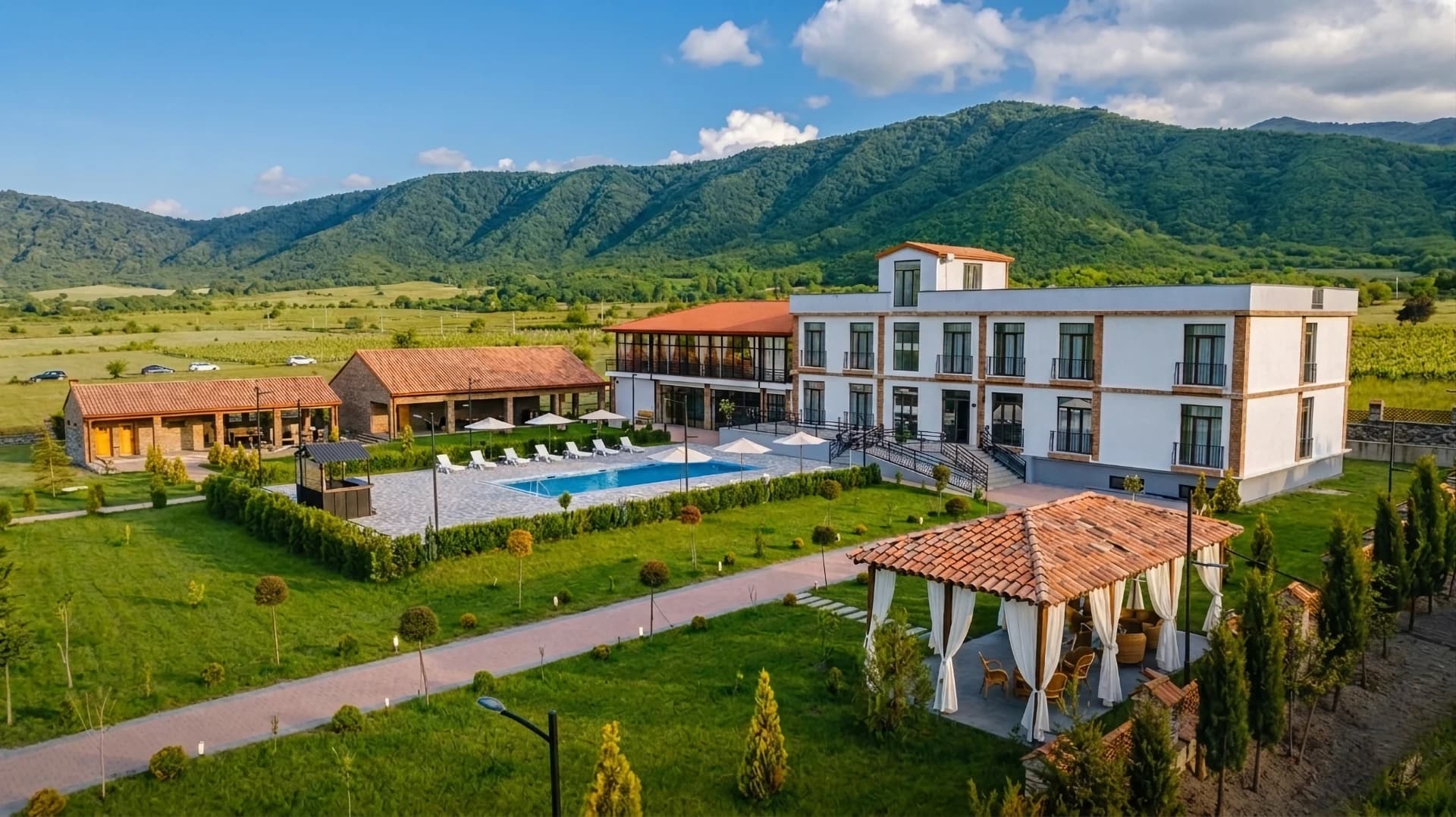 Hotel Inn Gremi mit Gartenwegen, Pool, Pavillons und bewaldeten Hügeln im Hintergrund