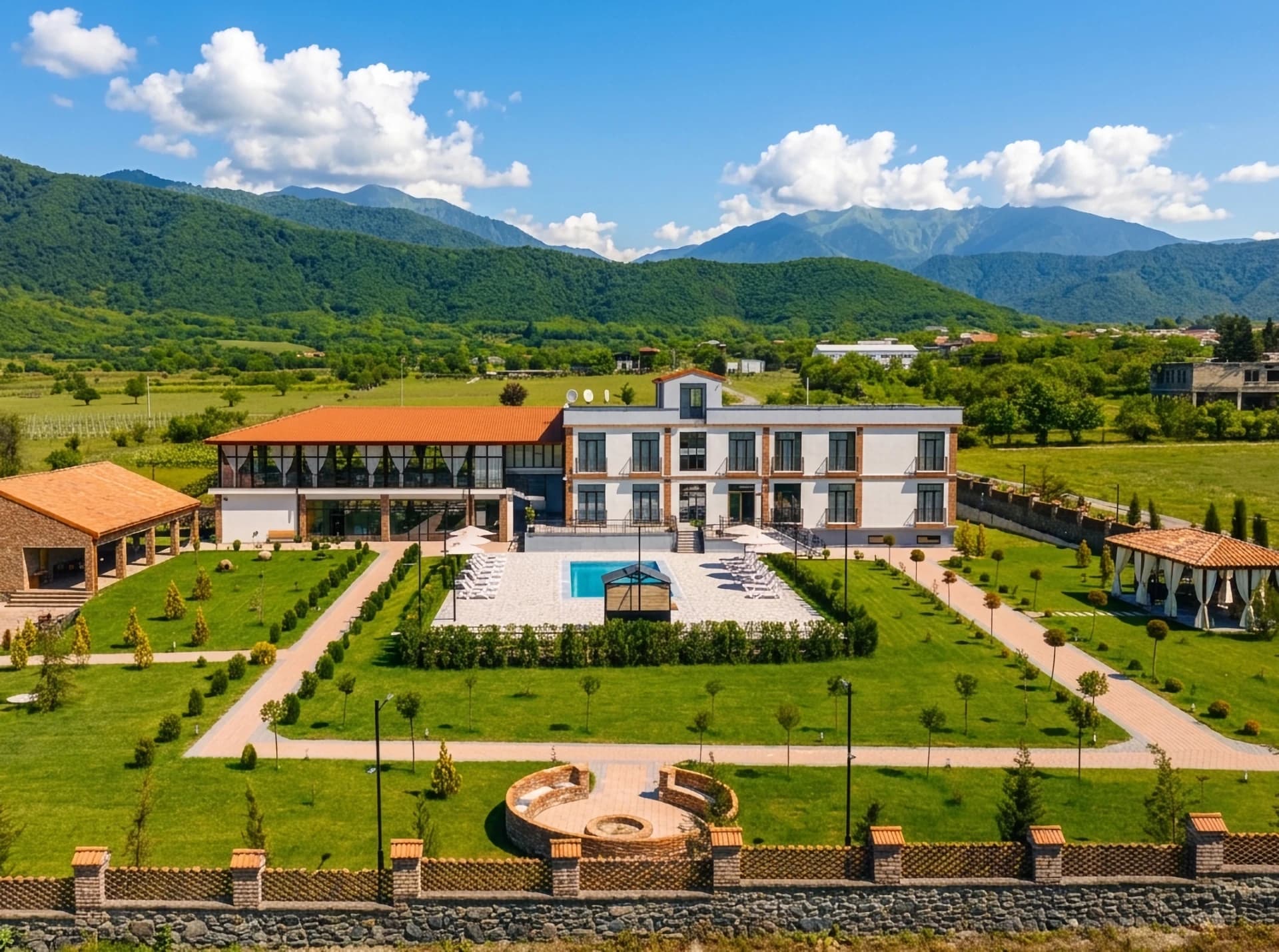 Frontansicht des Hotel Inn Gremi mit Pool, Garten und einer runden Feuerstelle im Vordergrund